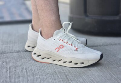 A close-up of a person's foot wearing white sneakers with coral accents and a unique sole design.